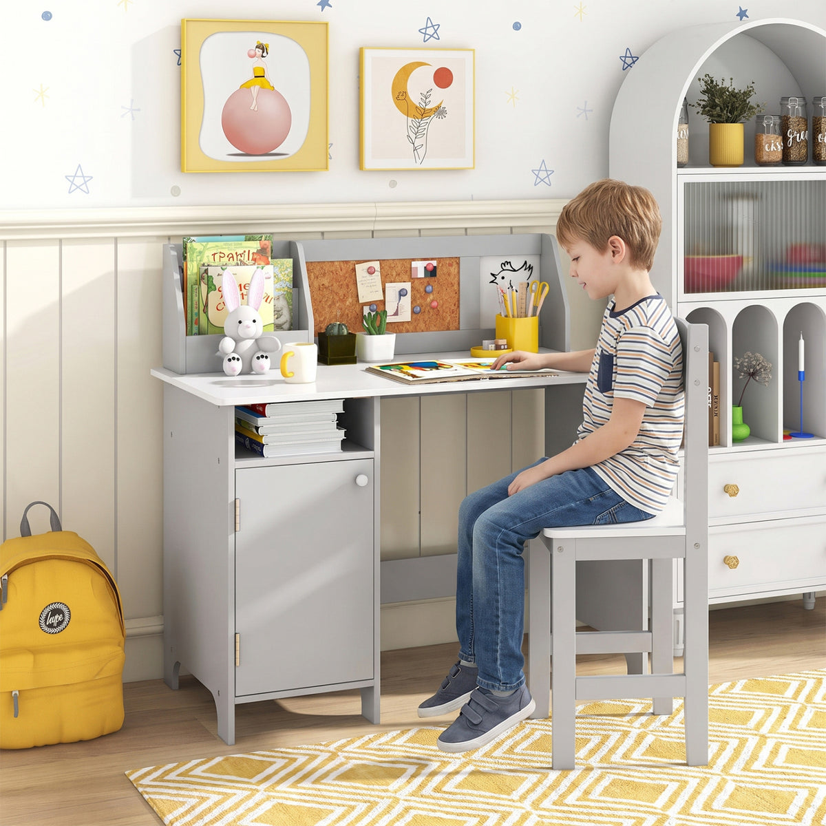 A child sits at a gray desk and chair, writing among books and school supplies.