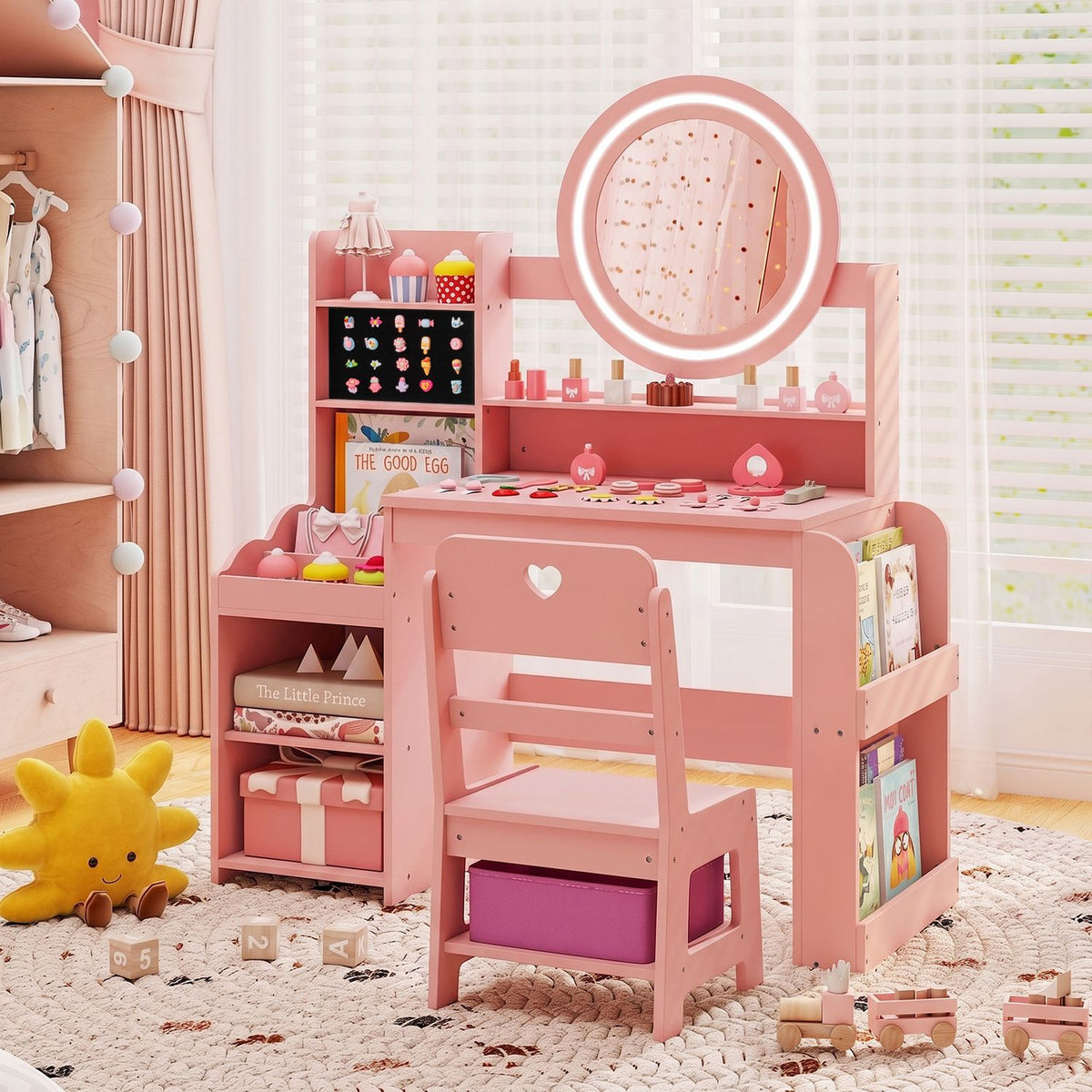 Pink kids’ vanity with a round lighted mirror, side shelves, and a matching chair in a bright bedroom.