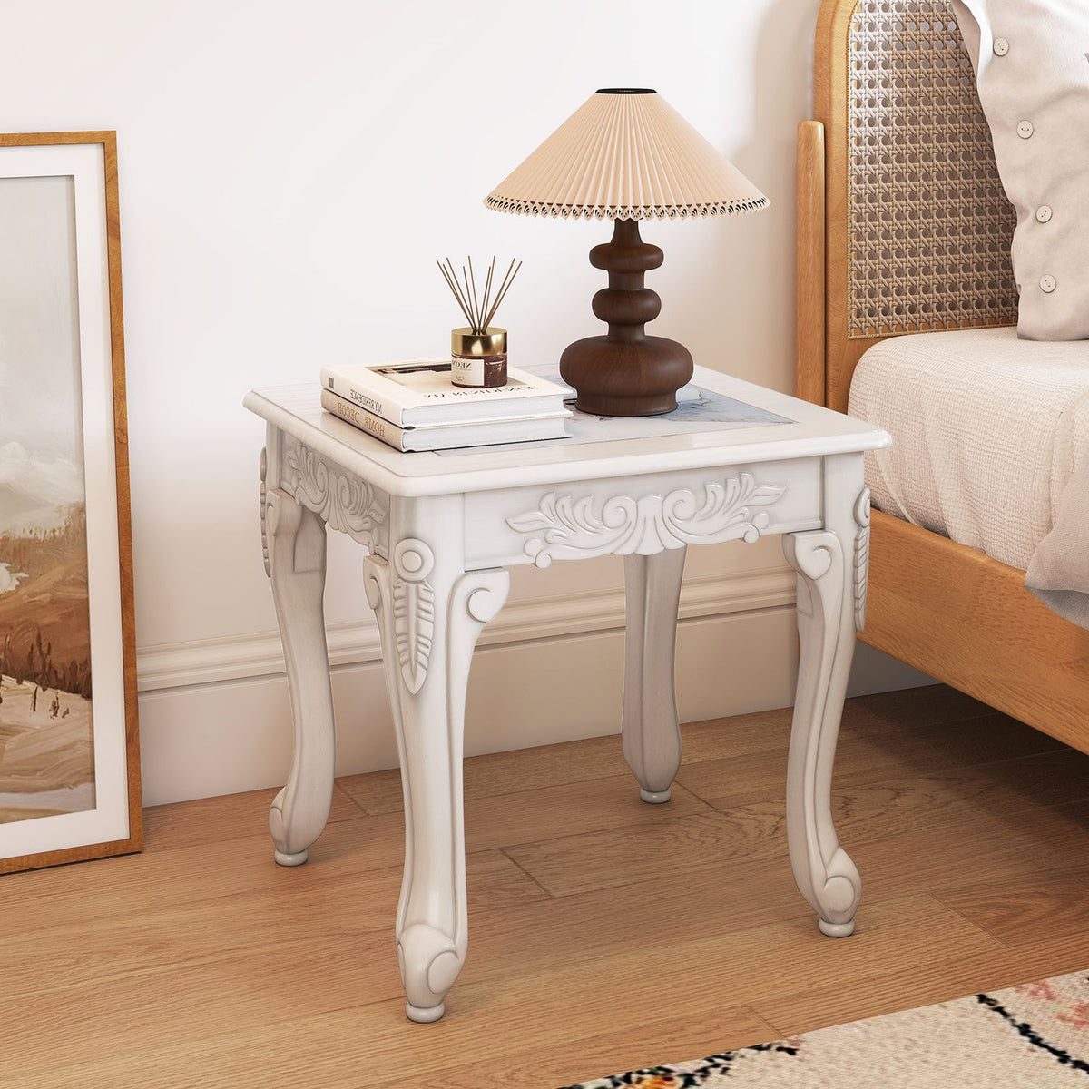 Carved white side table with a pale patterned top beside an upholstered chair in a warm-toned room.