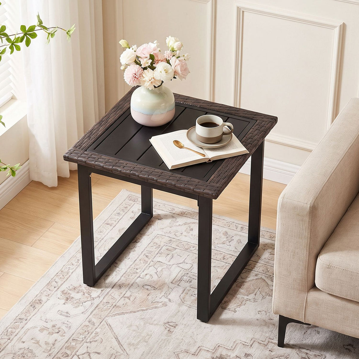 A dark side table beside an upholstered chair, styled with flowers, a coffee cup, and an open book.