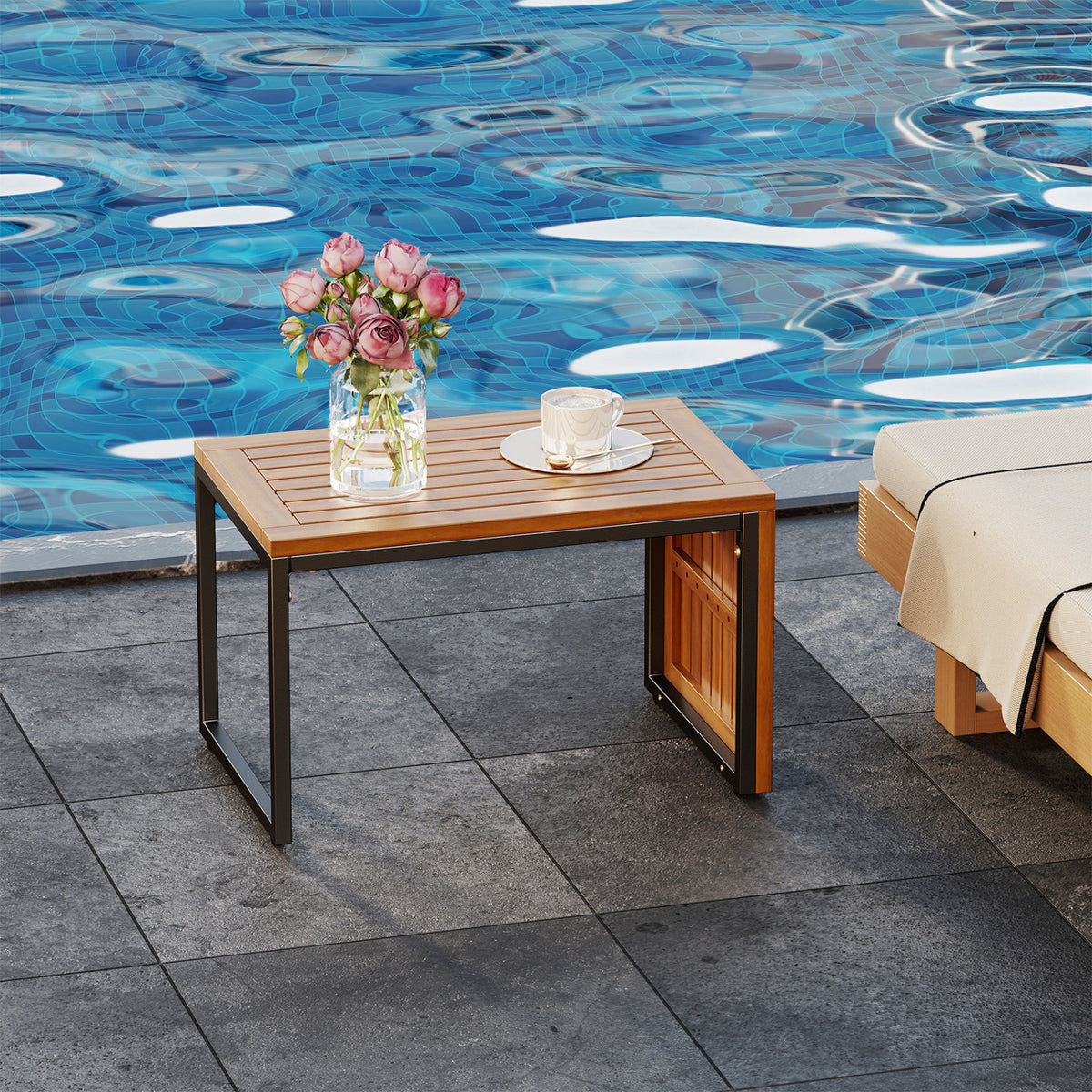 Wood-and-black-metal side table beside a pool, with flowers and a cup on top.