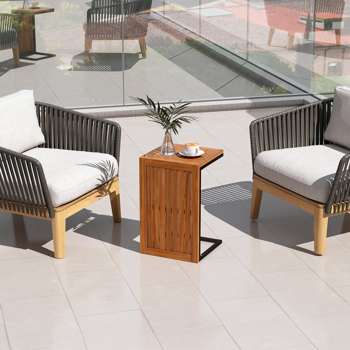 Upright wooden side table between two cushioned patio chairs, with a vase and cup on top.