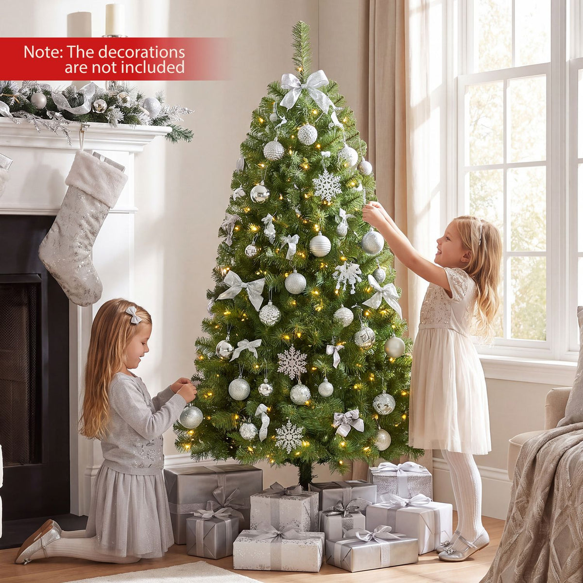 Two children decorate a lit Christmas tree with silver ornaments in a bright living room.
