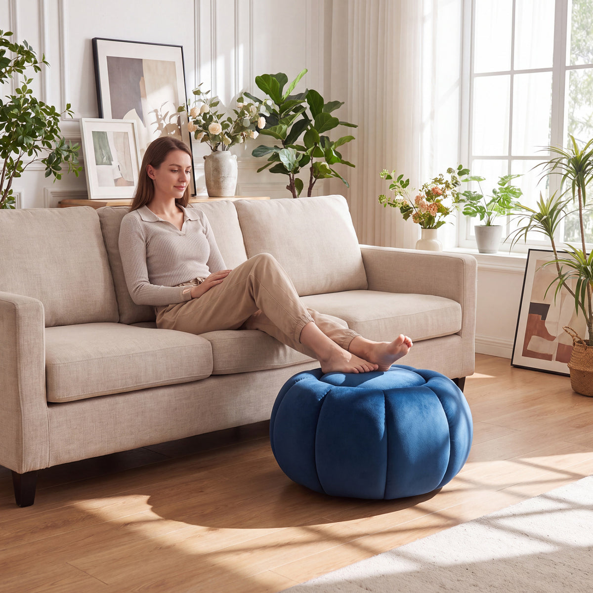 A woman rests her feet on a blue pumpkin-shaped ottoman beside a beige sofa.