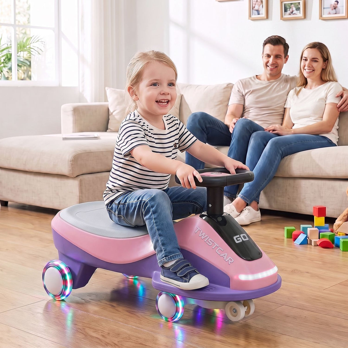 A child rides a pink and purple toy car with glowing wheel rings as two adults watch from a sofa.