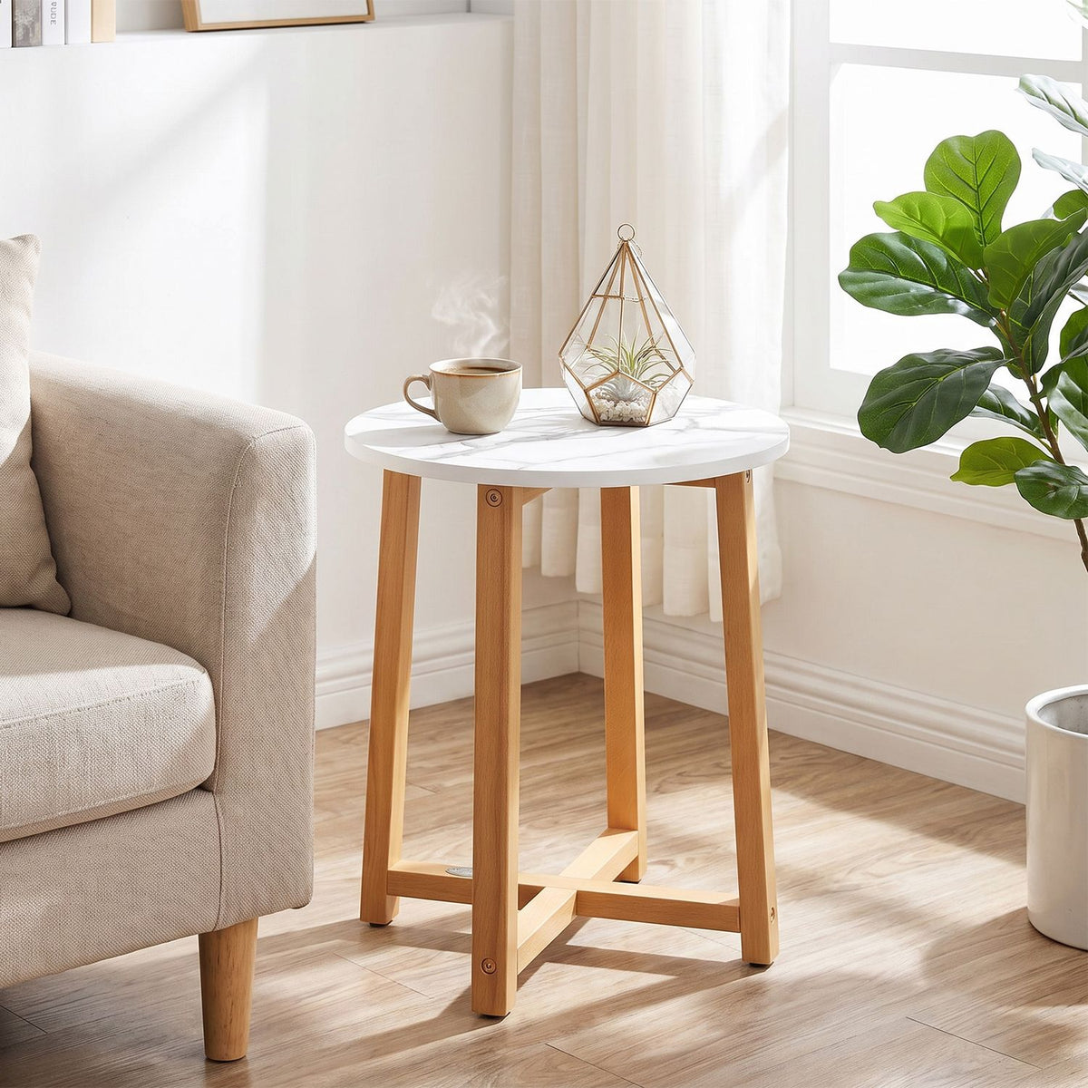 Round white marble-look table with wooden legs beside a sofa in a bright room.