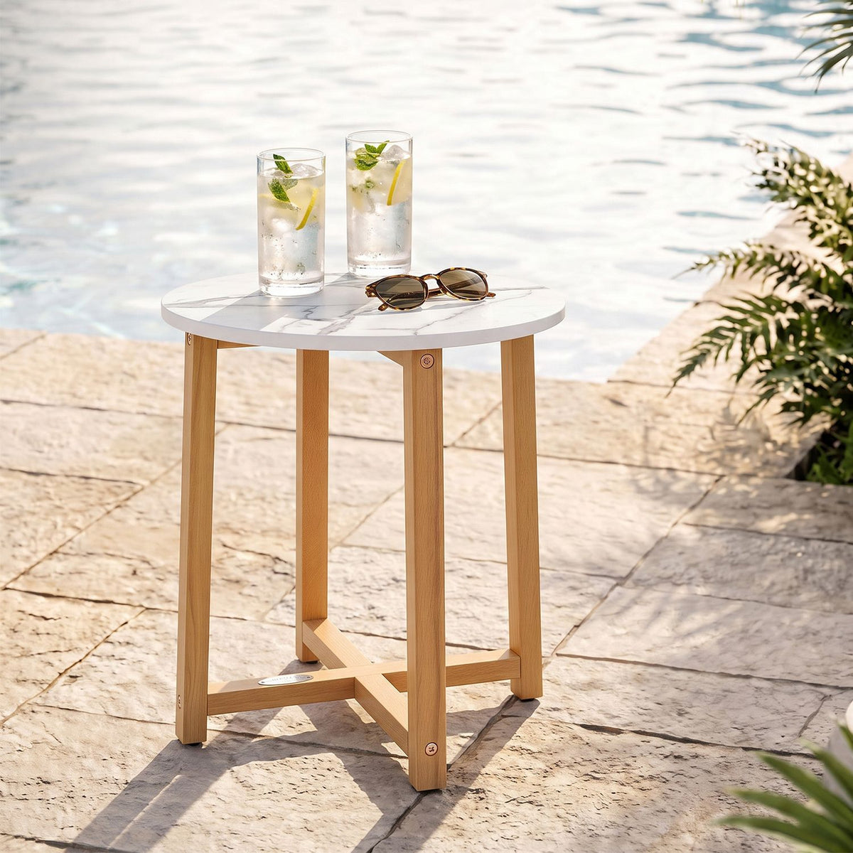 Round marble-look table with wooden legs beside a pool, topped with two drinks and sunglasses.