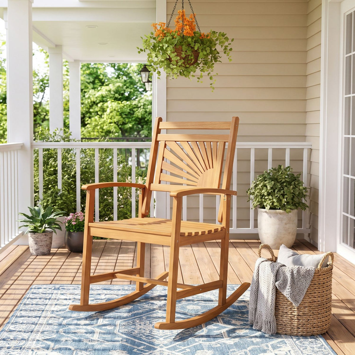A wooden rocking chair on a blue rug on a bright covered porch with potted plants and a hanging basket.