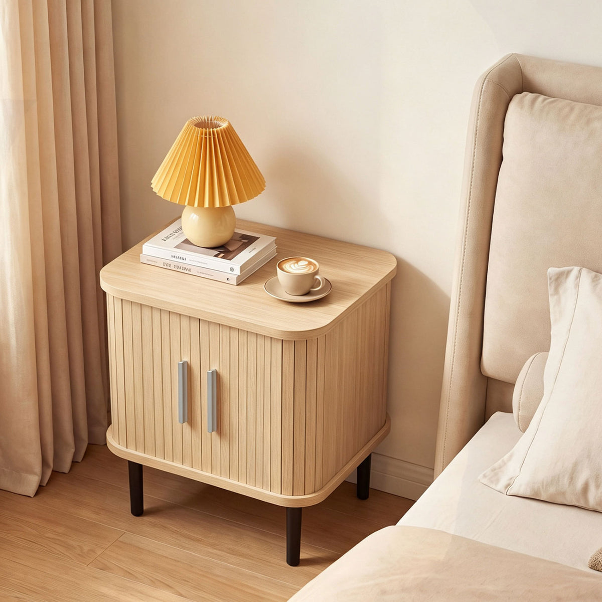 Closed fluted nightstand beside a bed, topped with a pleated lamp and a cup.
