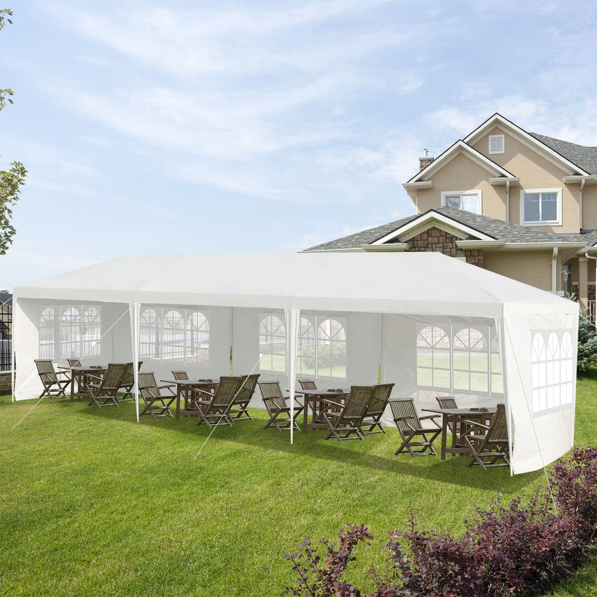 White canopy tent with windowed sidewalls shelters wooden tables and chairs on a lawn.