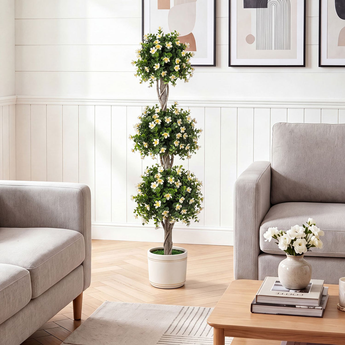 Green topiary tree with white flowers displayed between two sofas in a living room