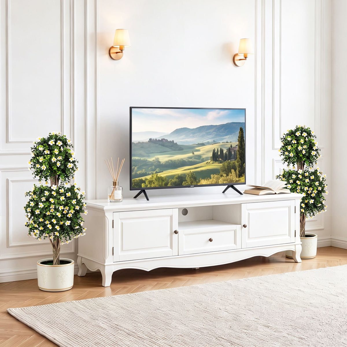 Two flowering topiary trees in pale planters stand beside a white media console.