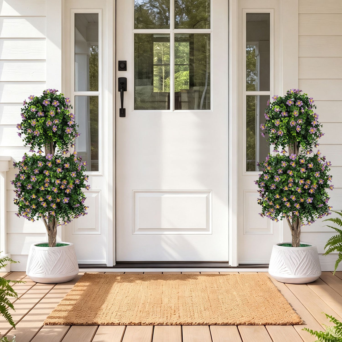 Matching flowering topiary trees in white planters flank a white front door.