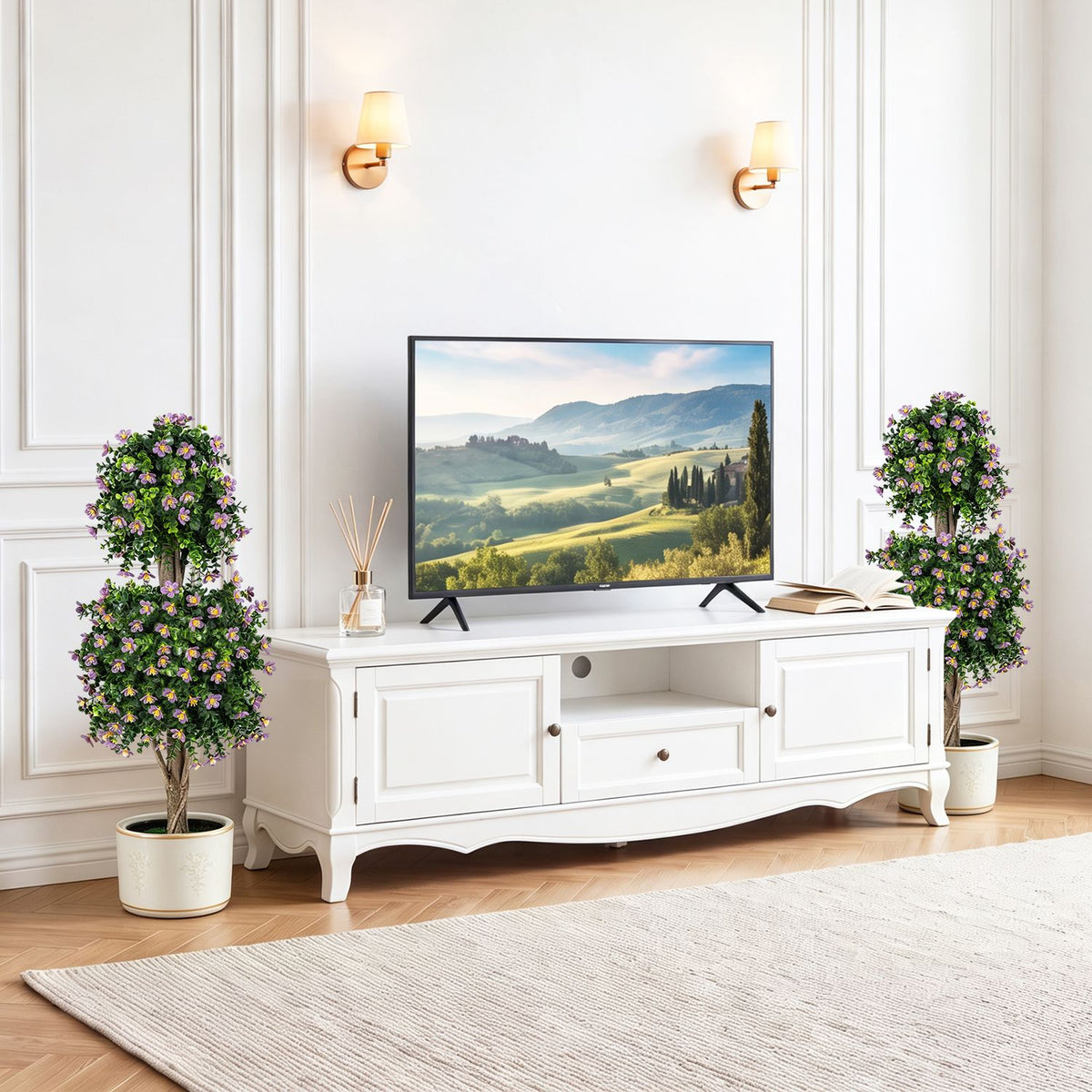 Two flowering topiary trees stand on either side of a white TV console.