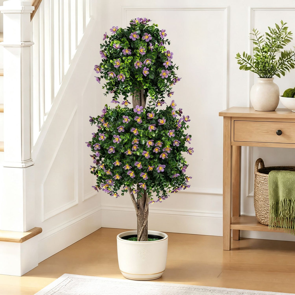 Flowering two-ball topiary in a white pot beside a staircase and wooden console.
