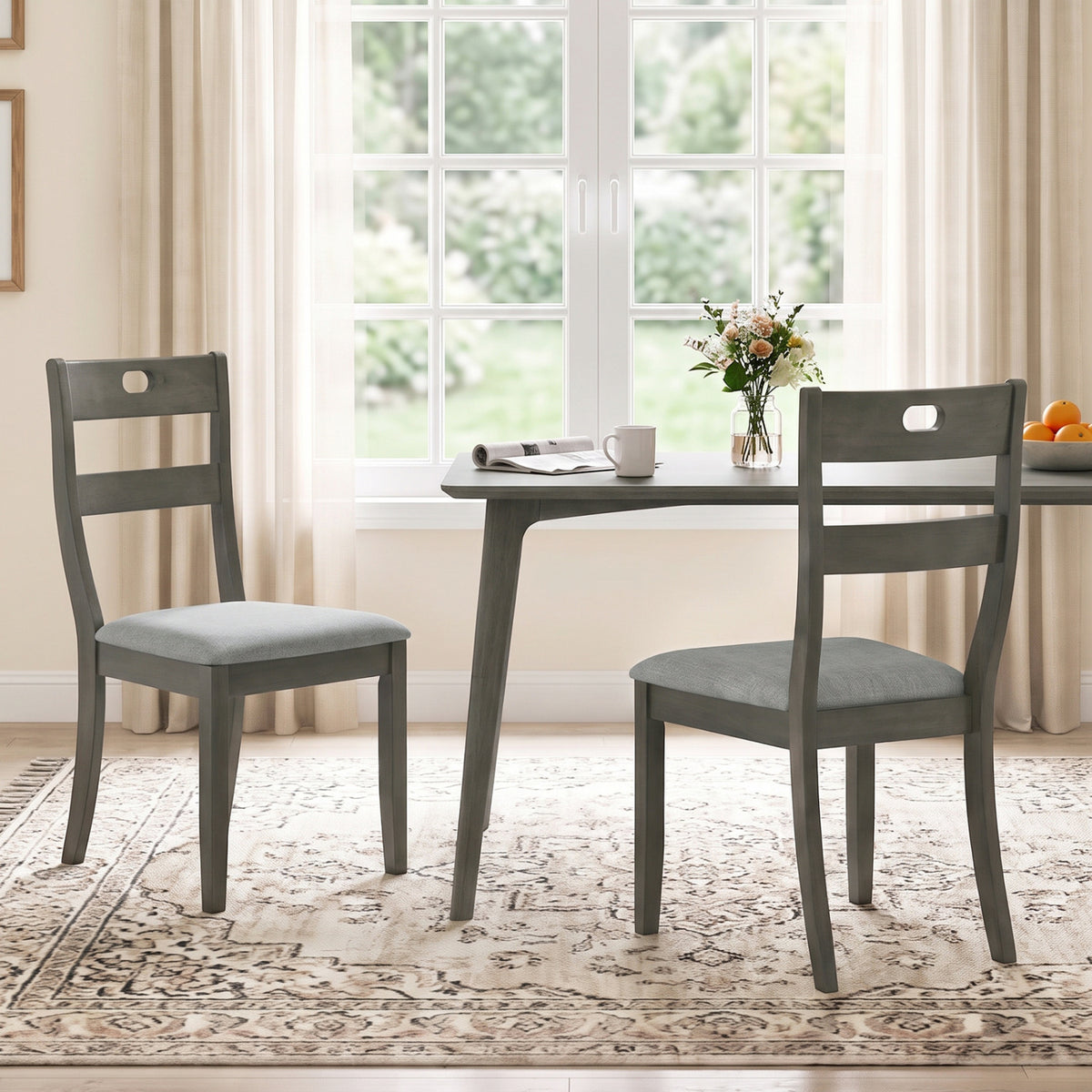 Two gray wooden ladder-back chairs with light gray padded seats sit beside a dining table by a bright window.