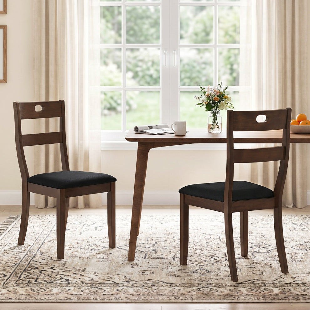 Two dark wood dining chairs with black padded seats beside a rectangular dining table by a bright window.