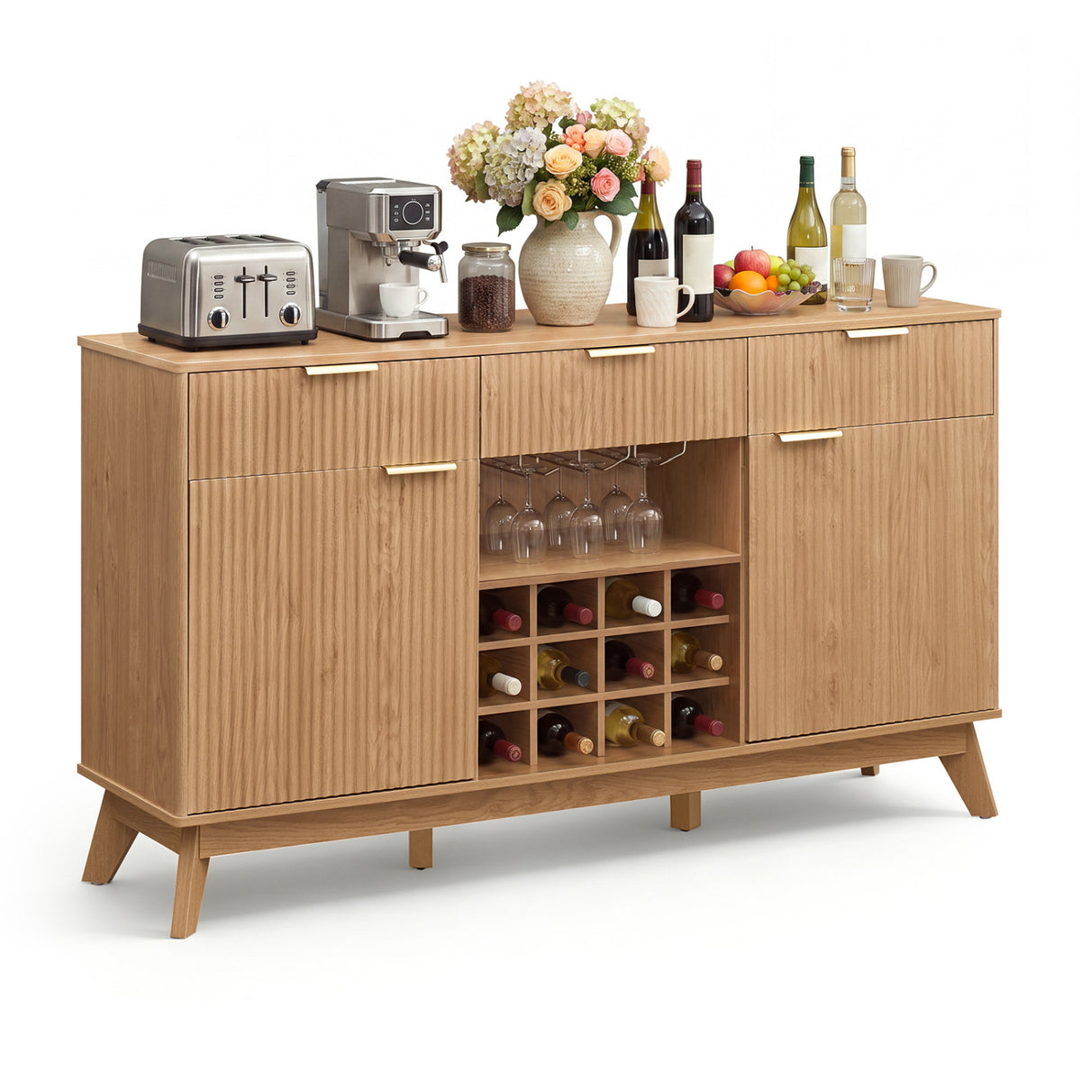 Fluted wood cabinet on a white background, topped with bottles, flowers, and kitchen items.