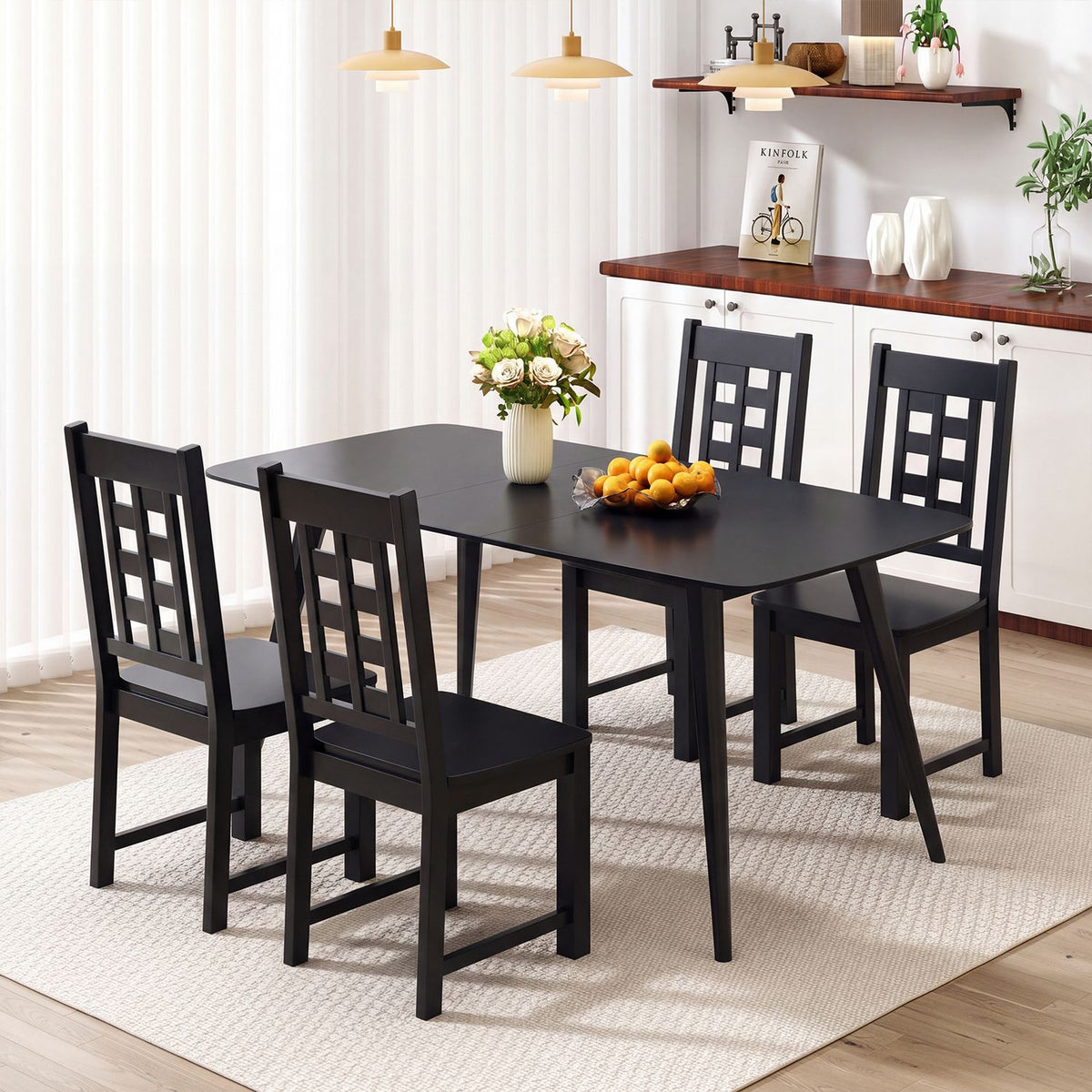 Four dark ladder-back chairs around a rectangular dining table beside a bright kitchen.