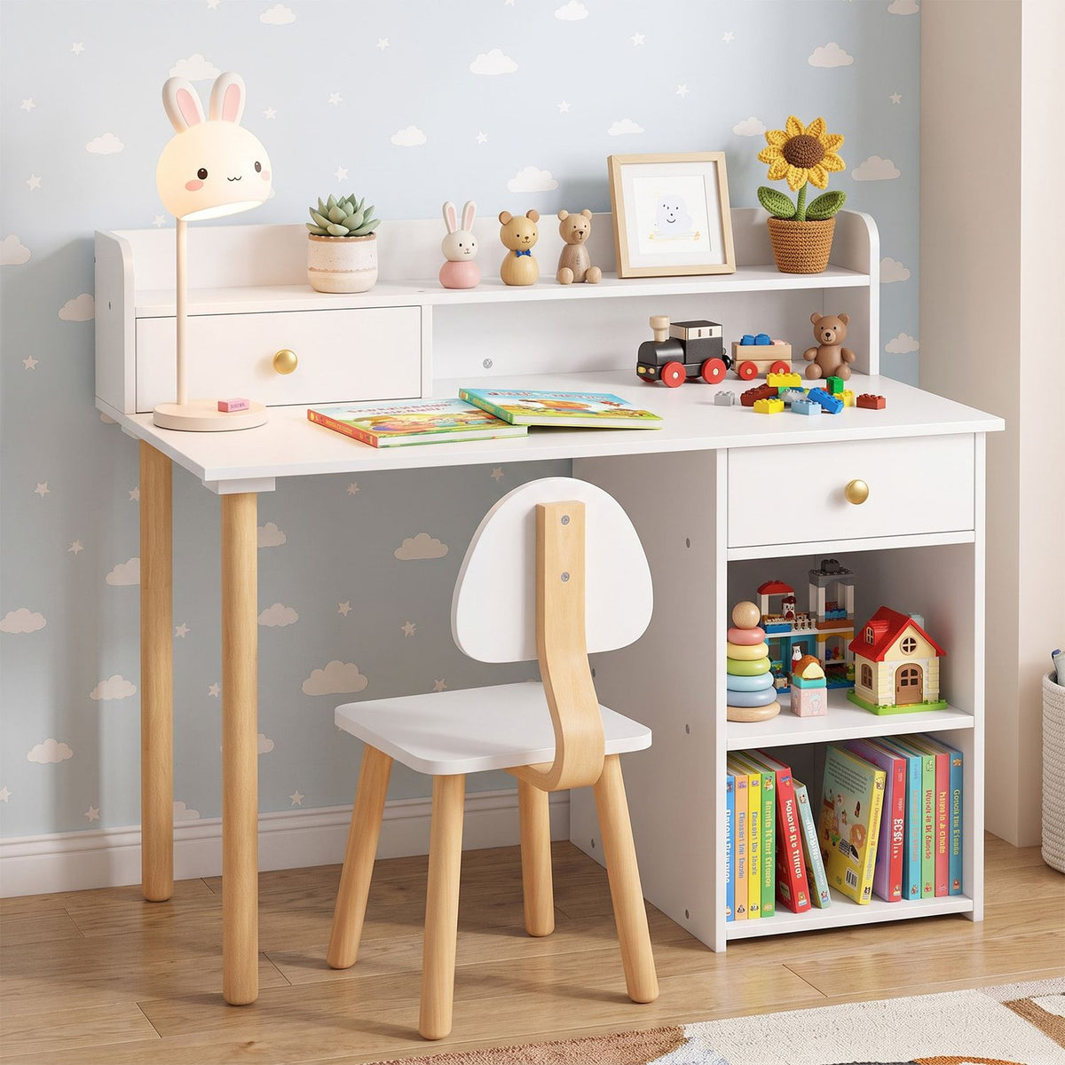 White kids’ desk and chair set styled with toys, books, and a sunflower in a patterned bedroom.