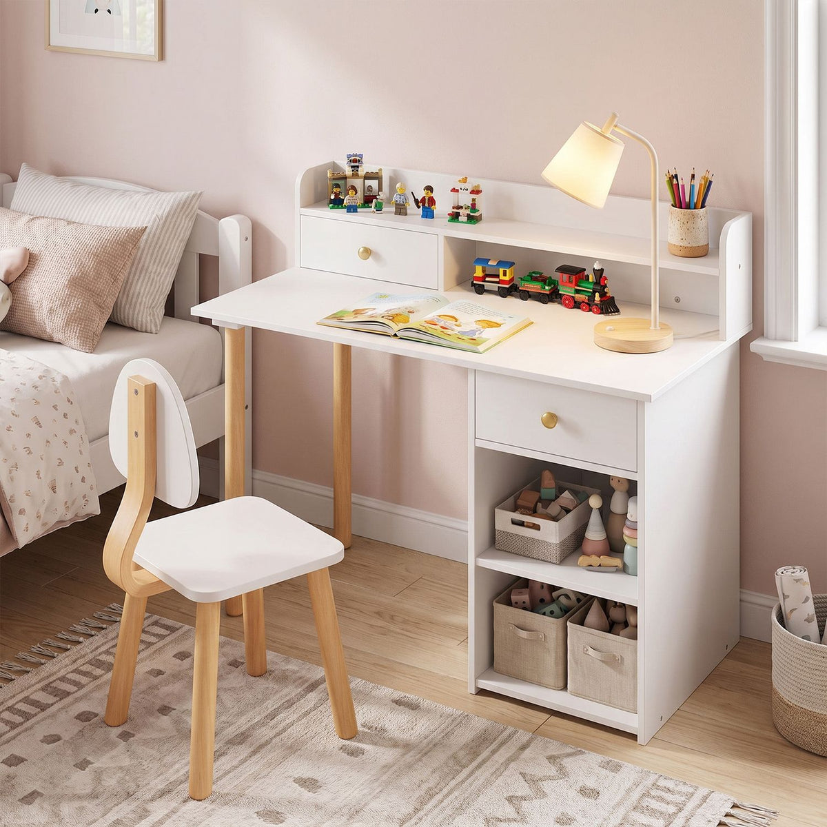 White children’s desk and chair beside a bed, with a lamp, toys, and storage baskets.