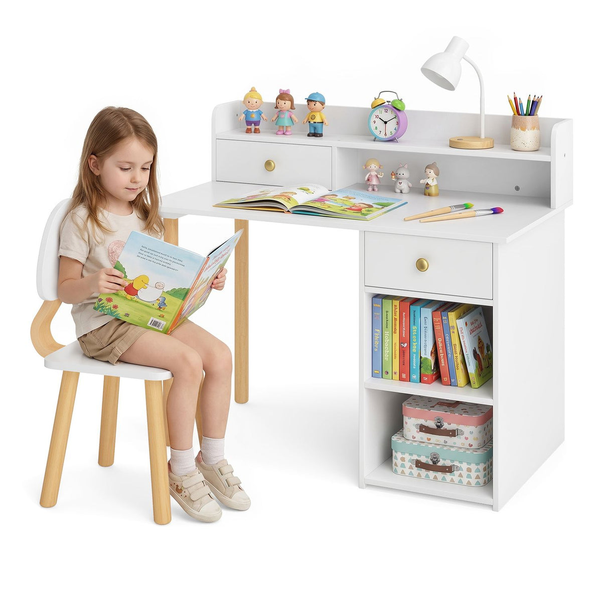 A child sits in the white desk chair reading beside the desk, which holds books and small toys.