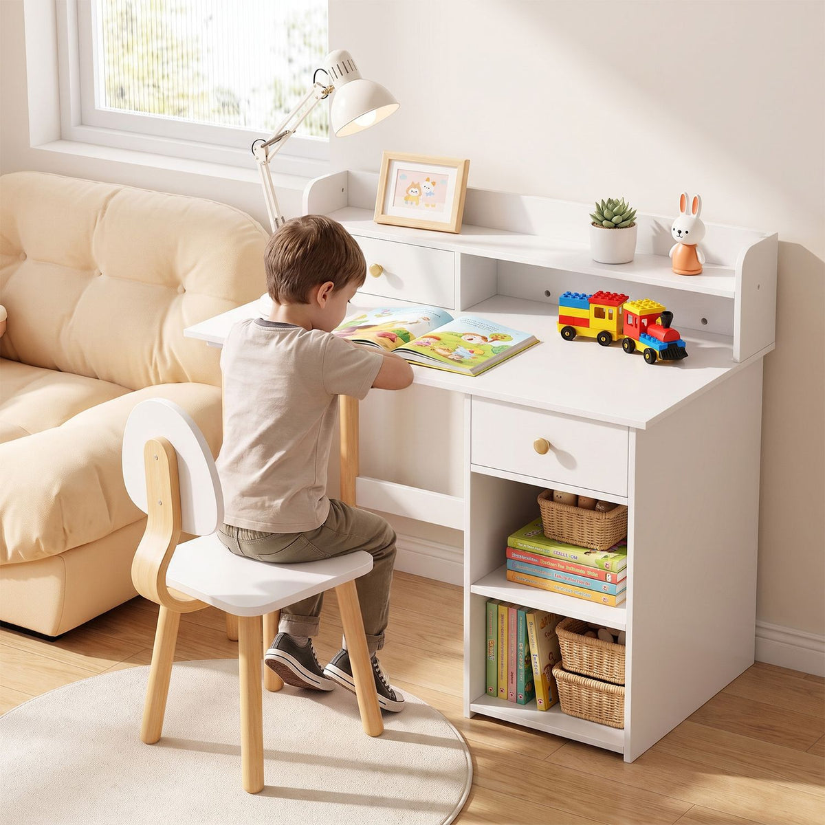 Child sits at a white desk and chair, reading beside toys, books, and storage shelves.
