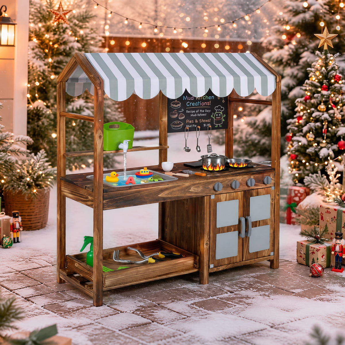 Wooden play kitchen with striped canopy and cookware, staged outdoors among snowy holiday decorations.