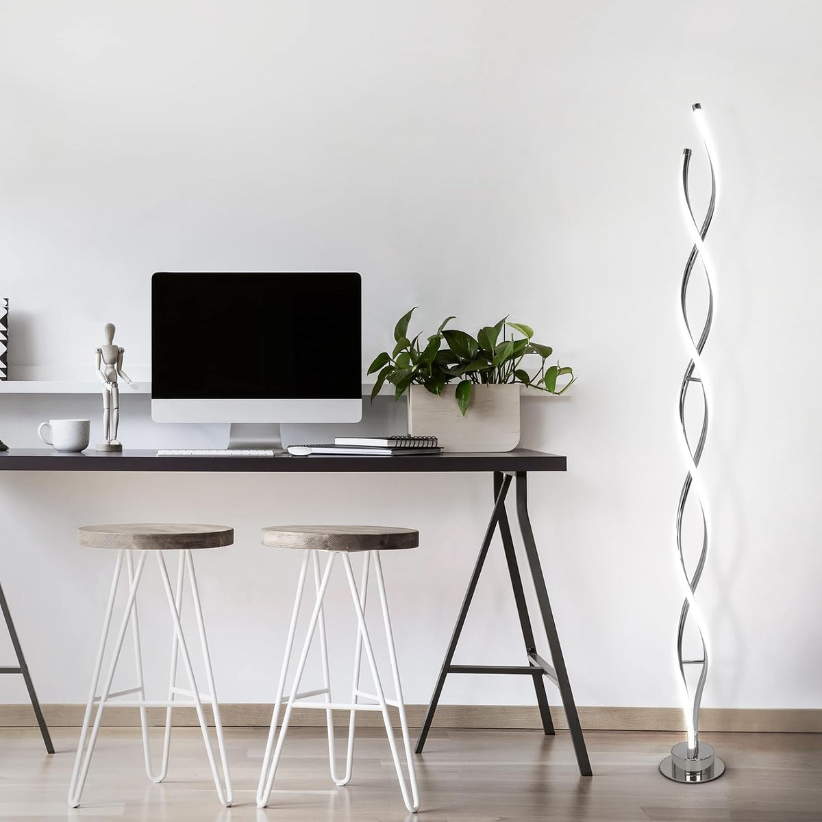 Slim spiral LED floor lamp illuminated beside a minimalist desk and two stools in a home office setting