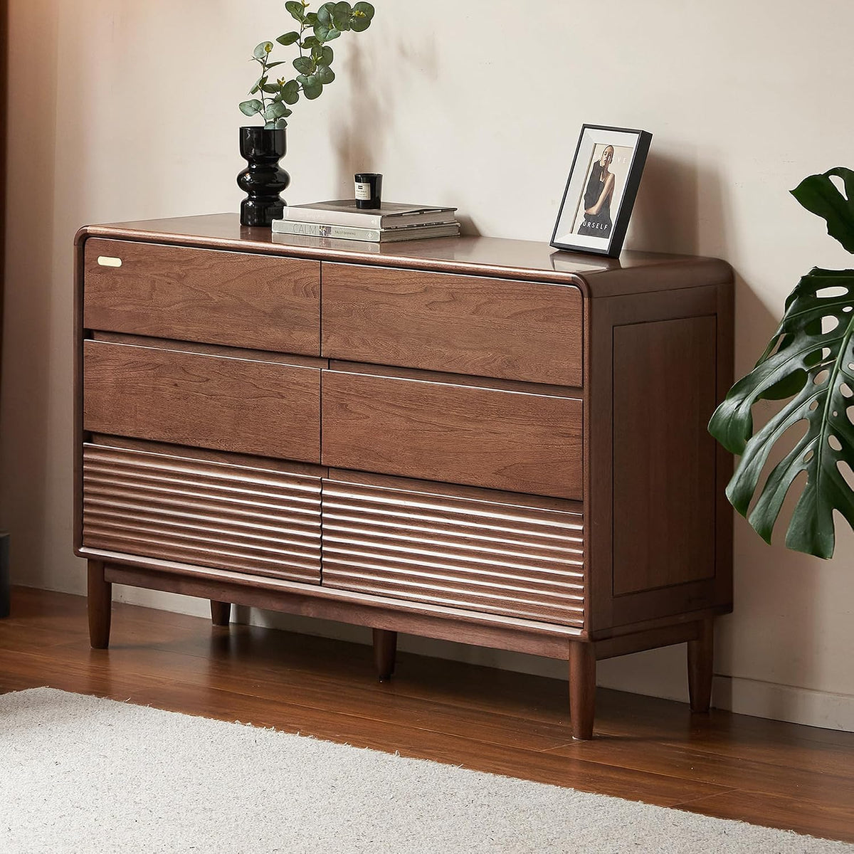 Three-quarter view of a mid-height dresser with smooth drawers and fluted lower panels, styled with books and a plant on top.