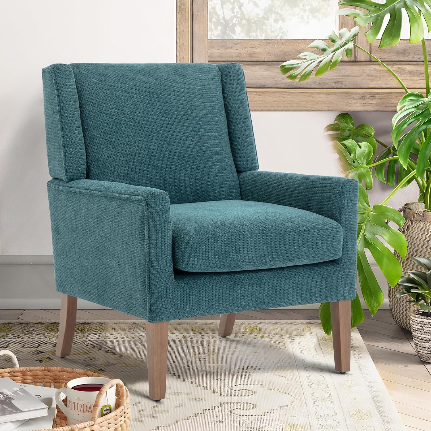 Single teal chenille wingback chair with light wood legs beside a window and potted plants