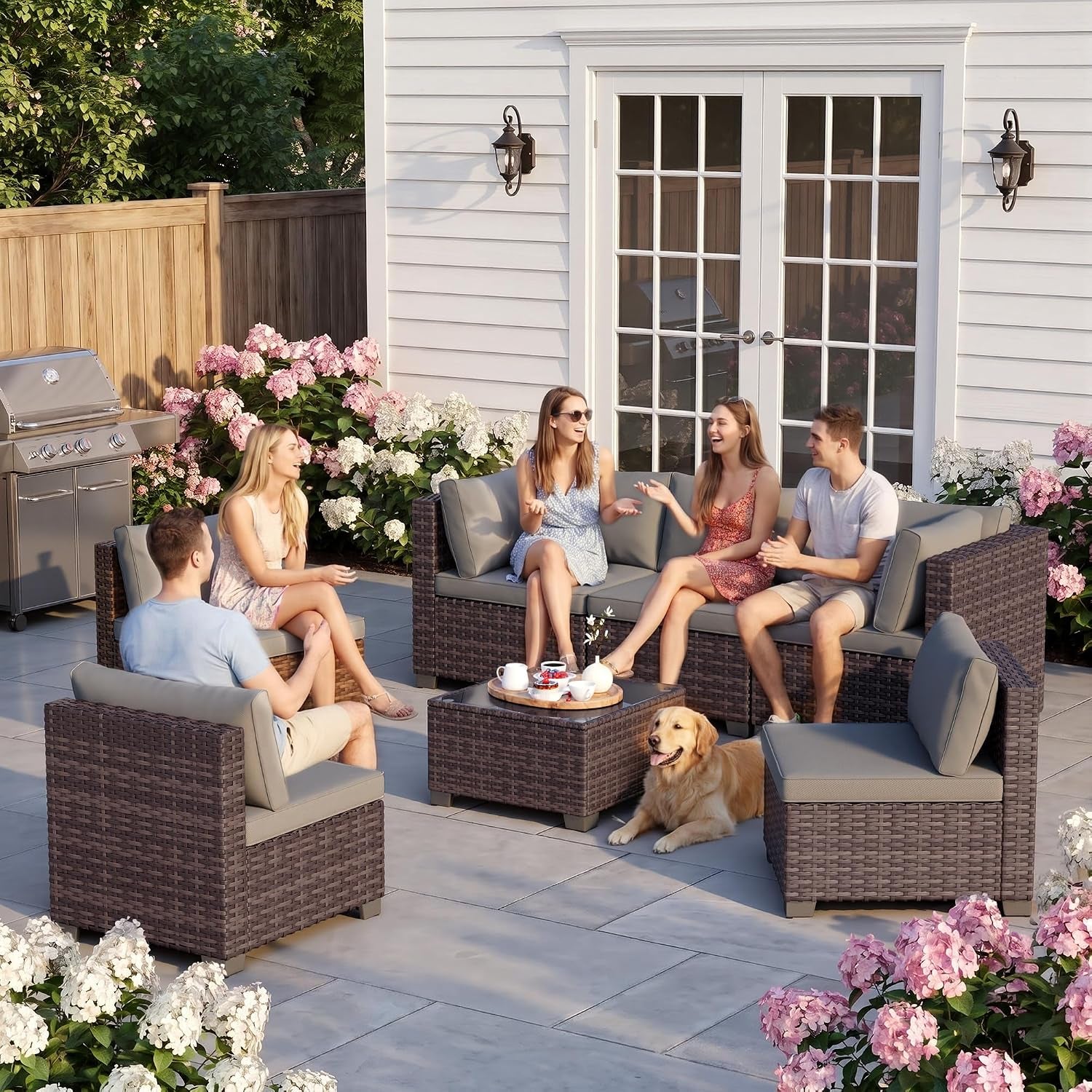 Group of friends sitting and chatting around a brown rattan patio seating set with a coffee table and a dog lying nearby.