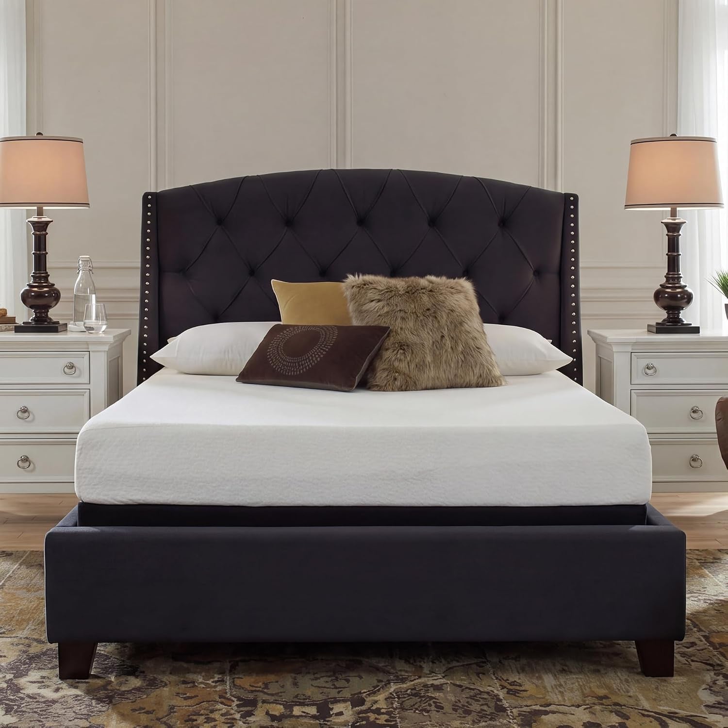 White mattress on a dark upholstered bed with tufted headboard, pillows, and matching nightstands with lamps.