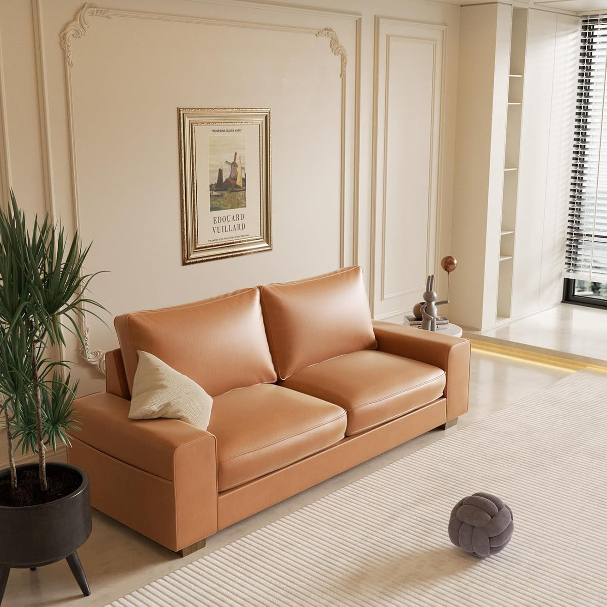 Angled view of the brown faux leather loveseat in a styled living room with wall art and a floor lamp.