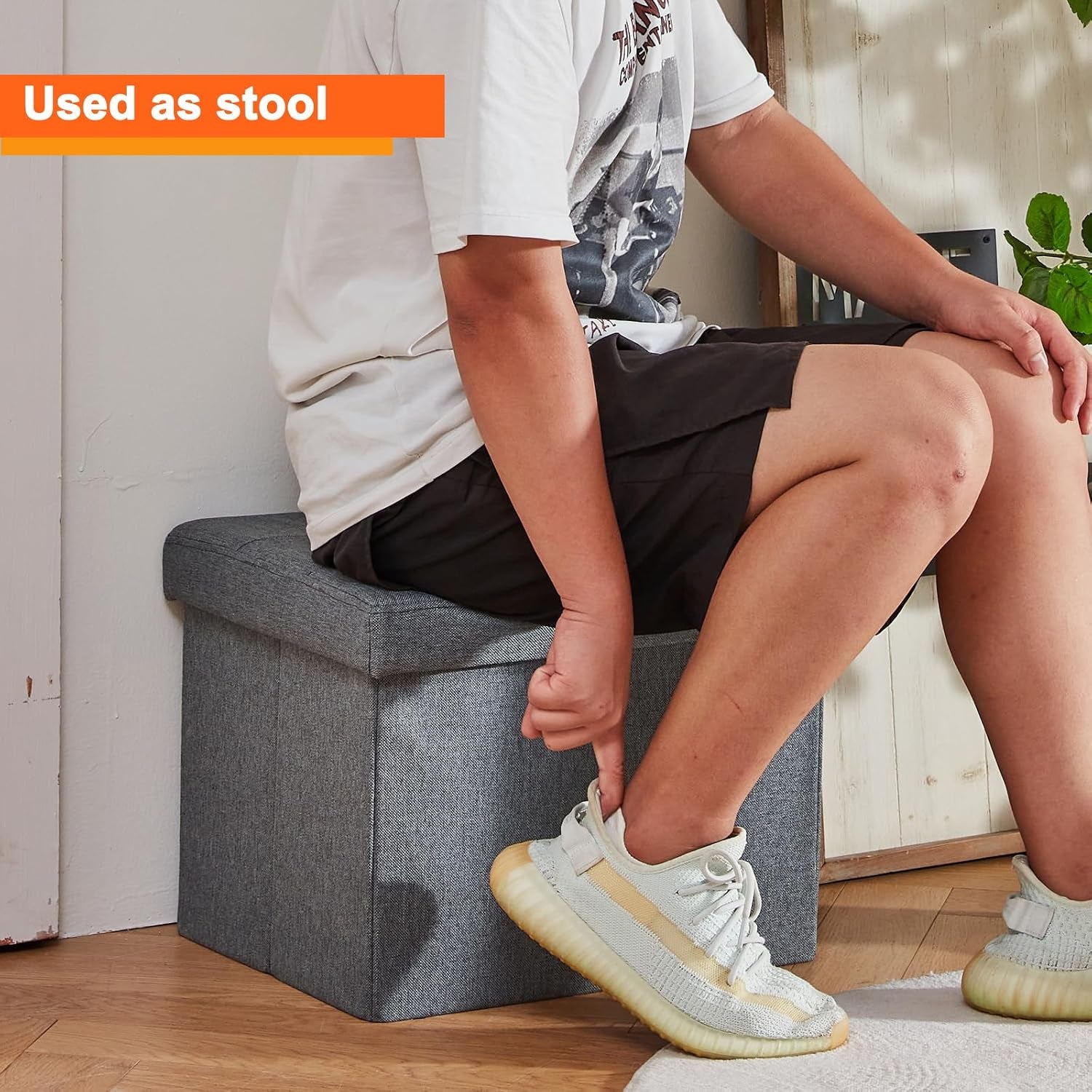 Person sitting on the grey ottoman used as a small stool in a casual room setting
