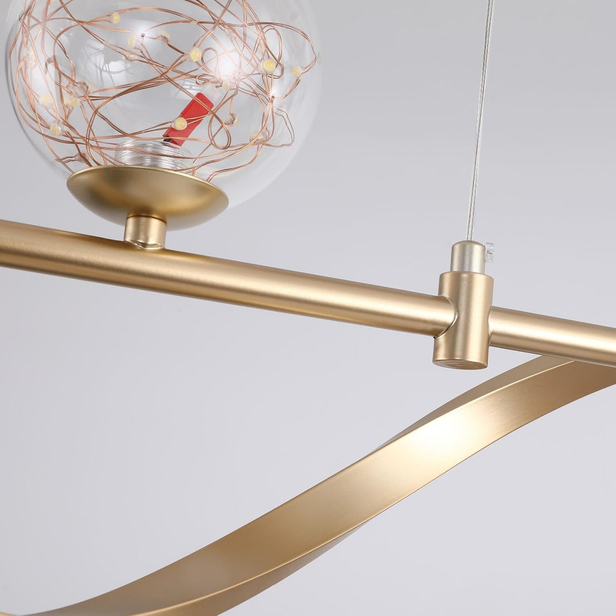 Close-up of gold metal rod and curved arm with clear globe shade holding wrapped LED wire.