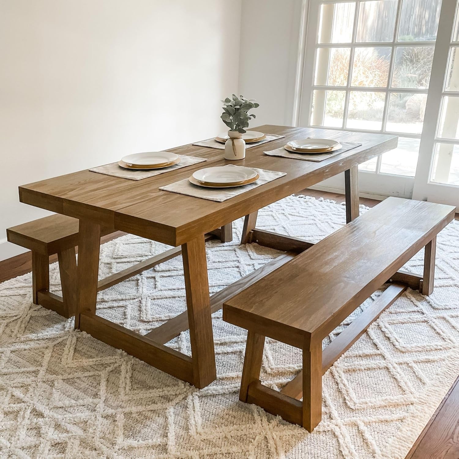Dining table styled with place settings and a matching bench at the side in a bright room