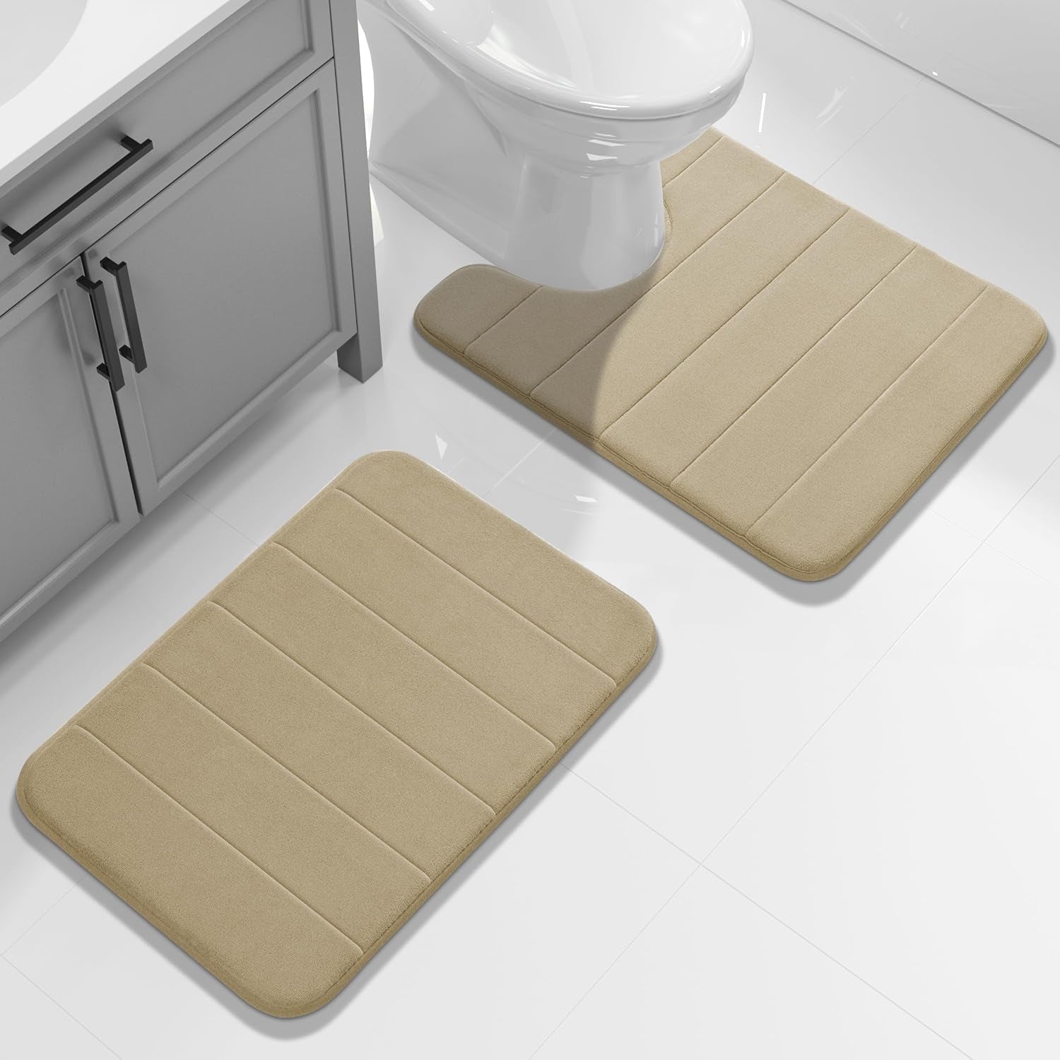 Beige two-piece bath mat set placed by a toilet and a vanity on white tile