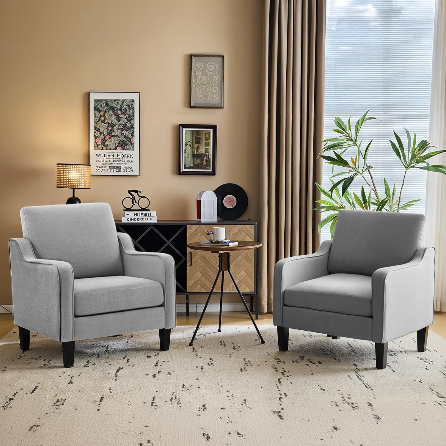 Two light grey upholstered armchairs flanking a small round wooden table in a cozy living room.