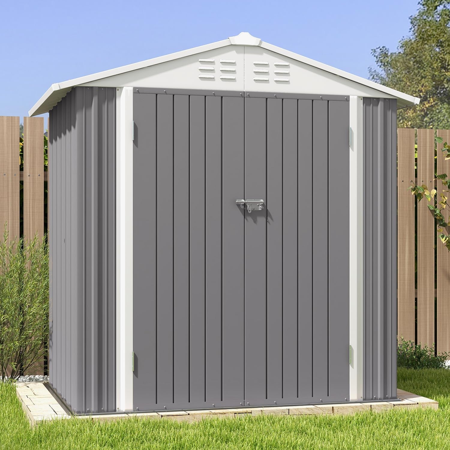 Front view of a gray metal storage shed with white peaked roof, double doors with latch, on grass by a wood fence.