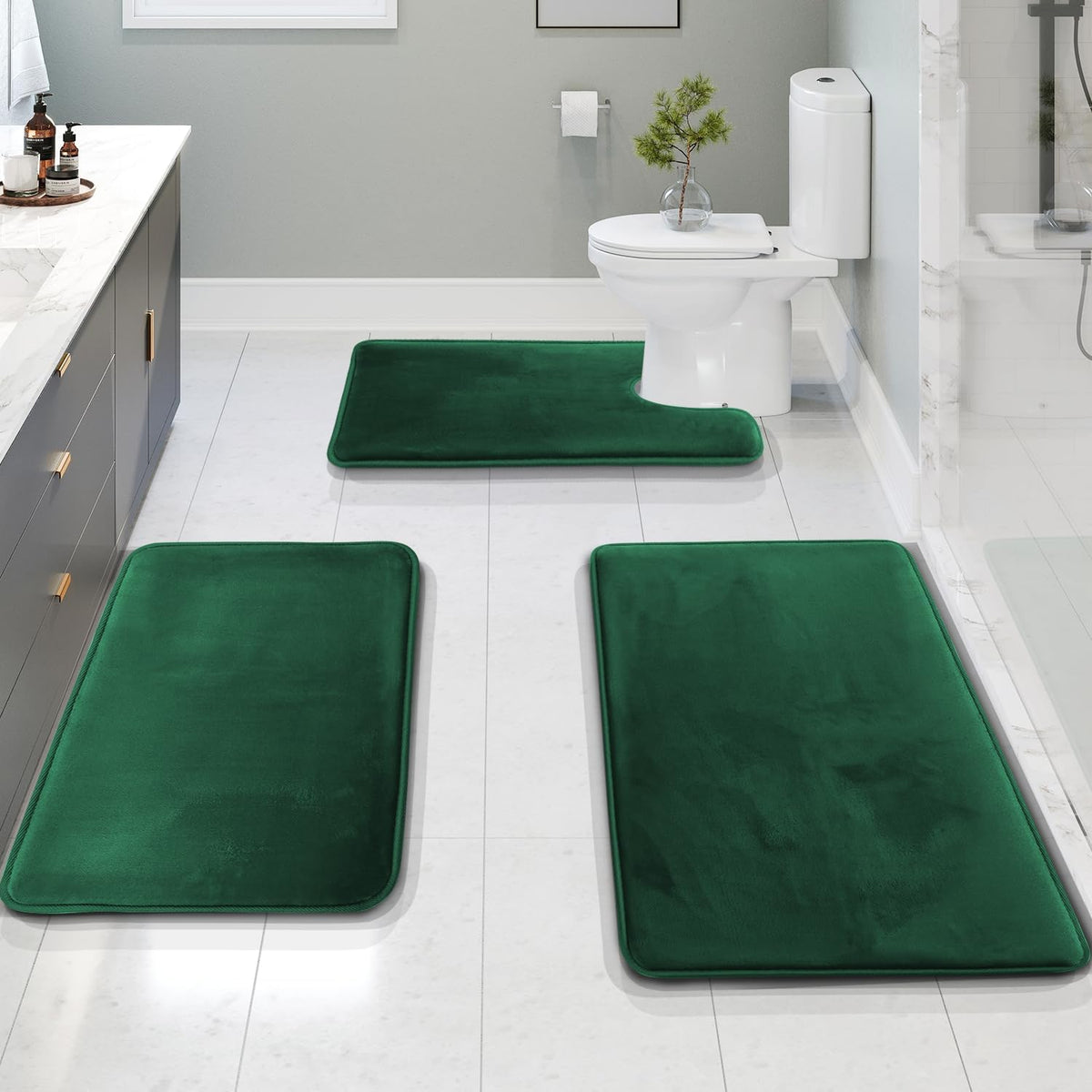 Three emerald-green bath rugs in a bathroom: two rectangular mats in foreground and a contour mat at the toilet.