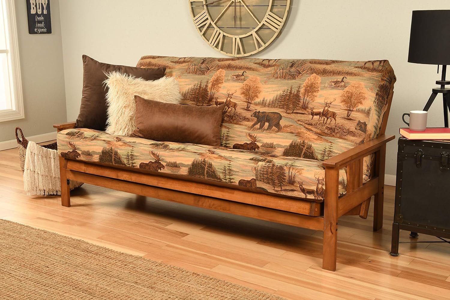 Full futon in a living room with tan wildlife tapestry cover on a mission-style hardwood frame and decorative pillows.