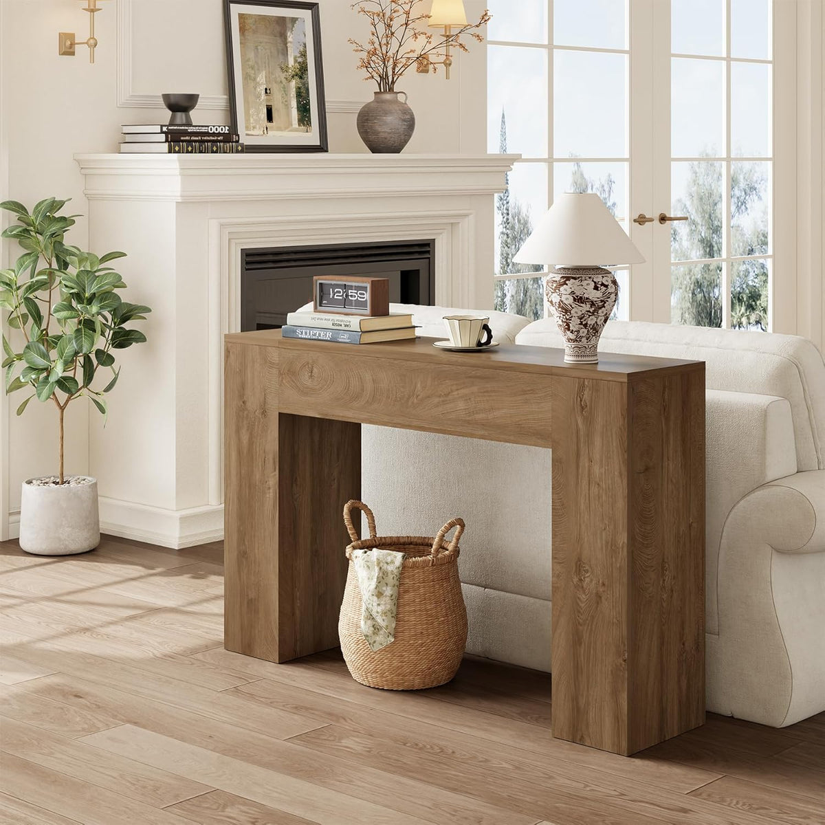 Console table placed behind a sofa in warm light oak finish with lamp, books and small clock on top