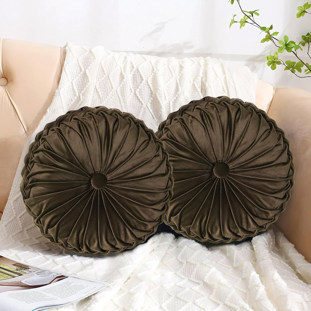 Close-up of two round dark-brown ruched pillows resting on a textured cream throw.