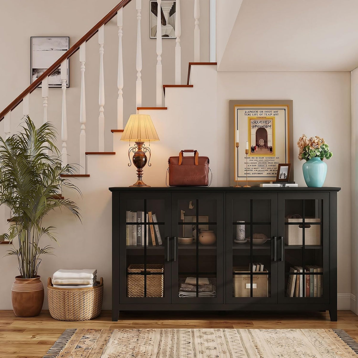 Black four-door glass-front buffet tucked beneath a staircase, topped with a lamp, framed print, bag and blue vase.