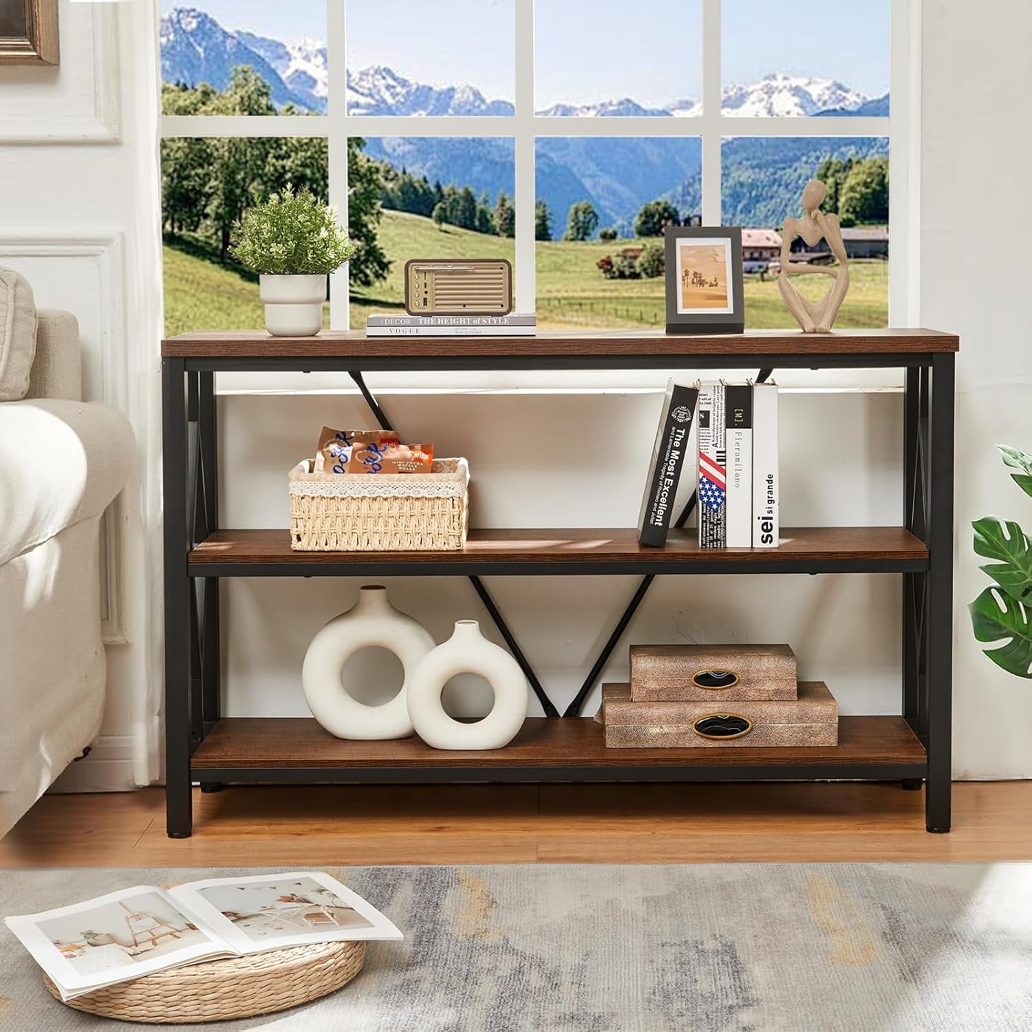 Three-tier rustic brown console beside a sofa, woven basket and two round white vases on shelves, open book on floor.