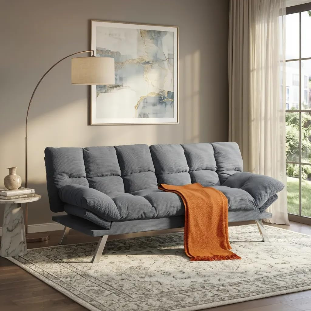 Three-seat gray velvet futon sofa in a styled living room with orange throw draped over the seat.