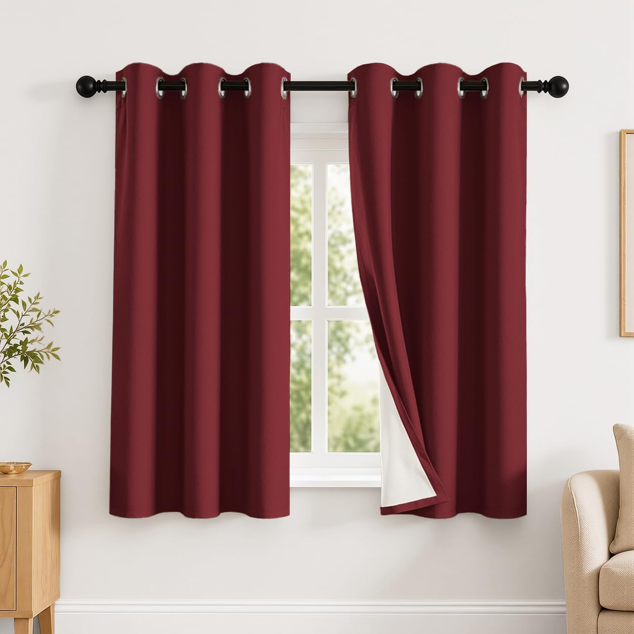 Window with two deep red grommet curtains, right panel pulled back to reveal white backing.