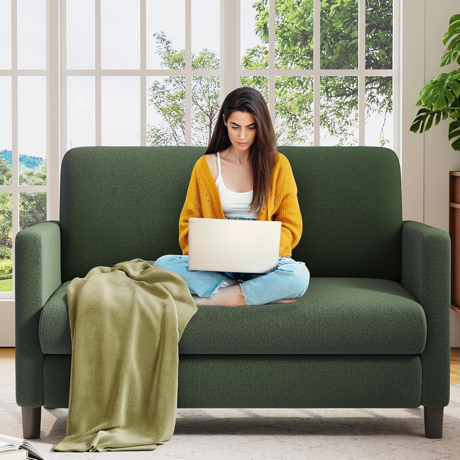 Green two-seat loveseat with a woman using a laptop and a draped blanket