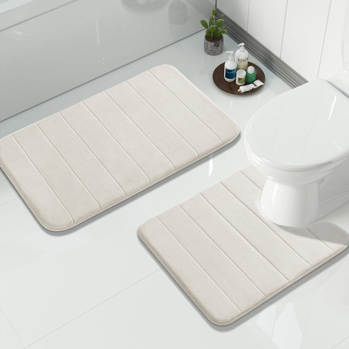 Top-down bathroom scene showing two cream-beige rectangular bath mats near tub and toilet